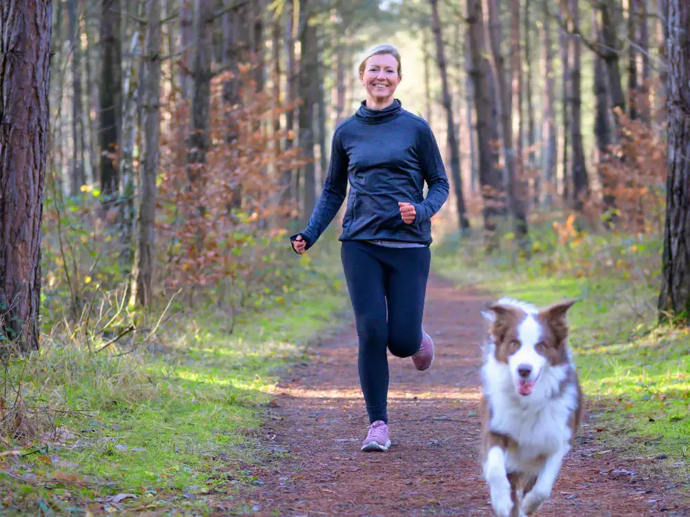 A woman and medium sized dog going on a run in the forest